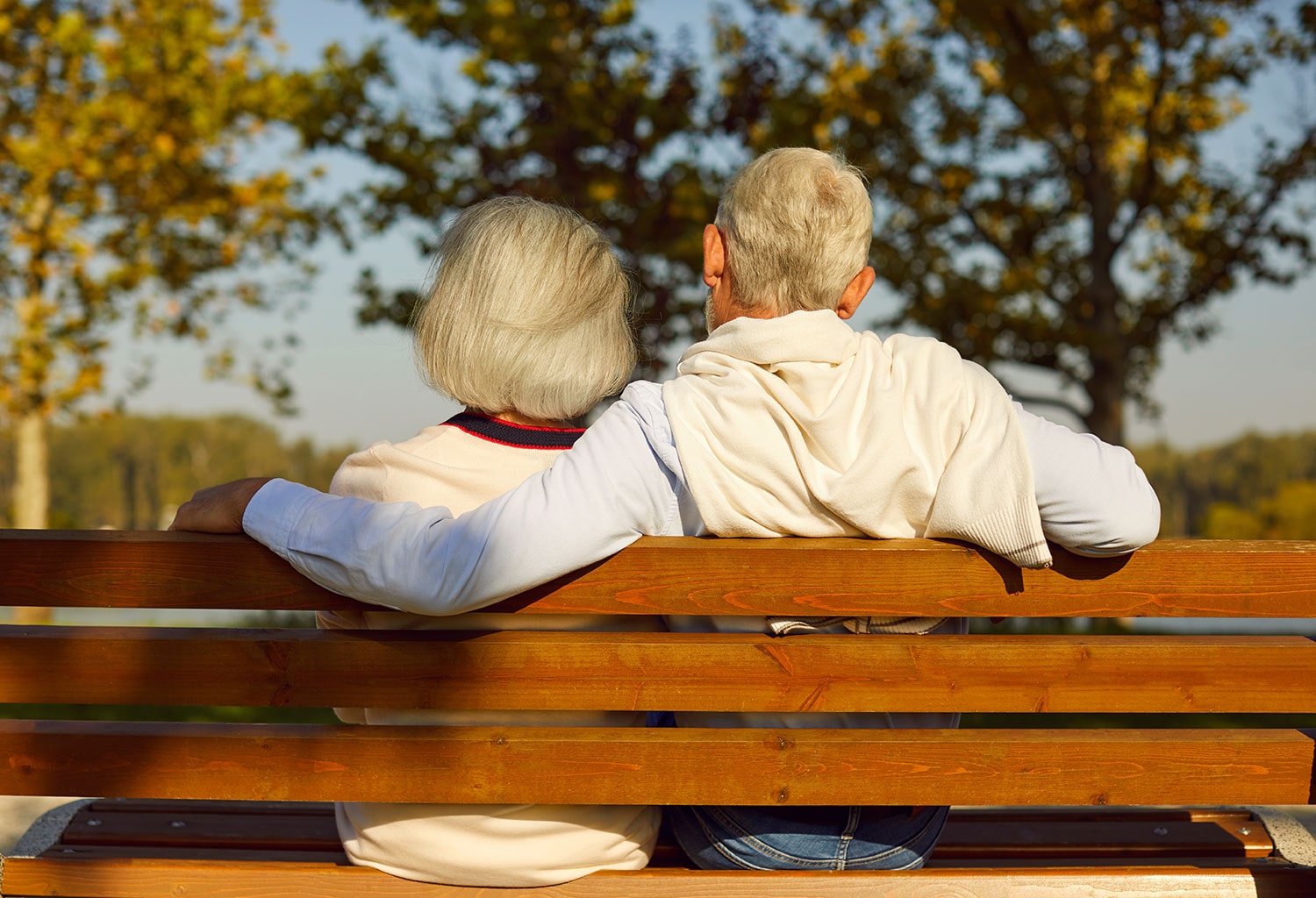 An image of an older couple sat down on a bench in the sun.