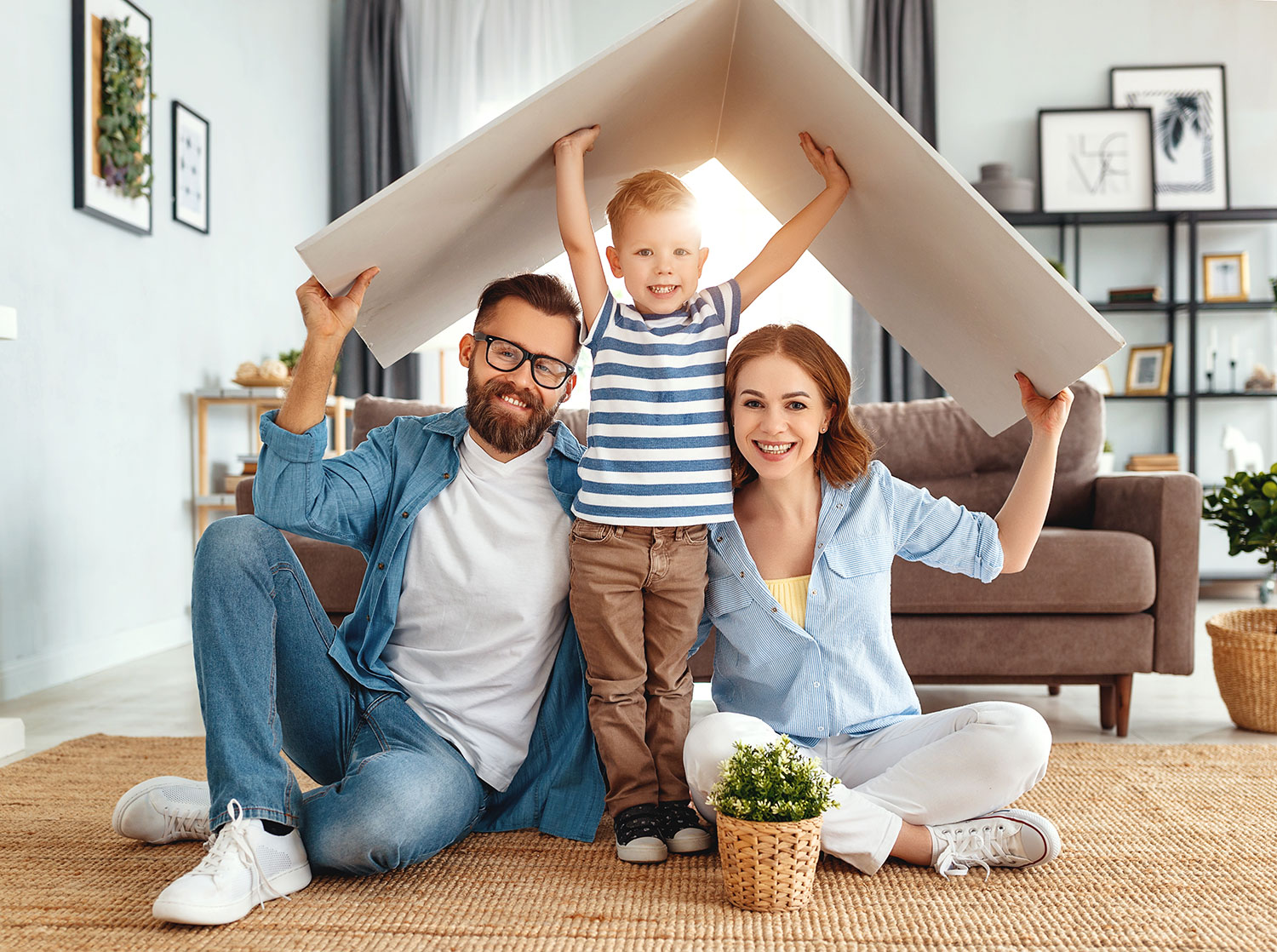 An image of a happy family holding a cardboard box like a roof over their heads.